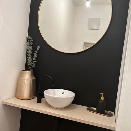 Badezimmer mit einer dunklen Wand und einem runden Spiegel